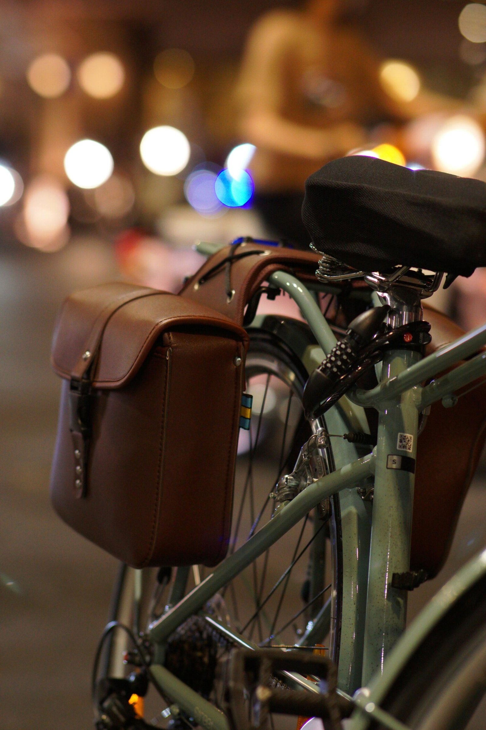 Close-up of a vintage bicycle with leather panniers on a city street at night.