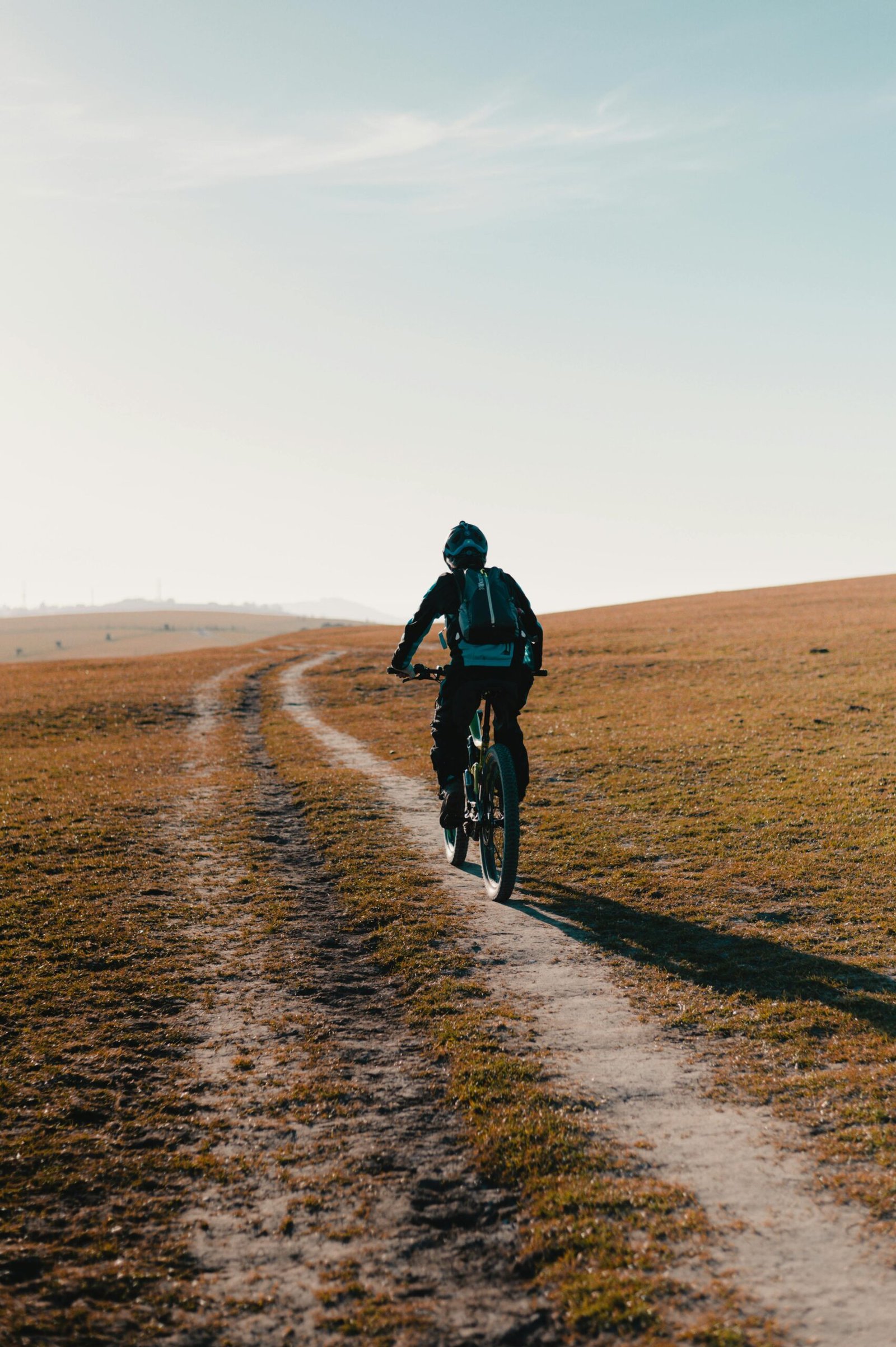 Cyclist riding a mountain bike on a winding dirt path through open landscape.